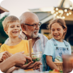 A grandfather holds his two smiling grandchildren on his lap.   